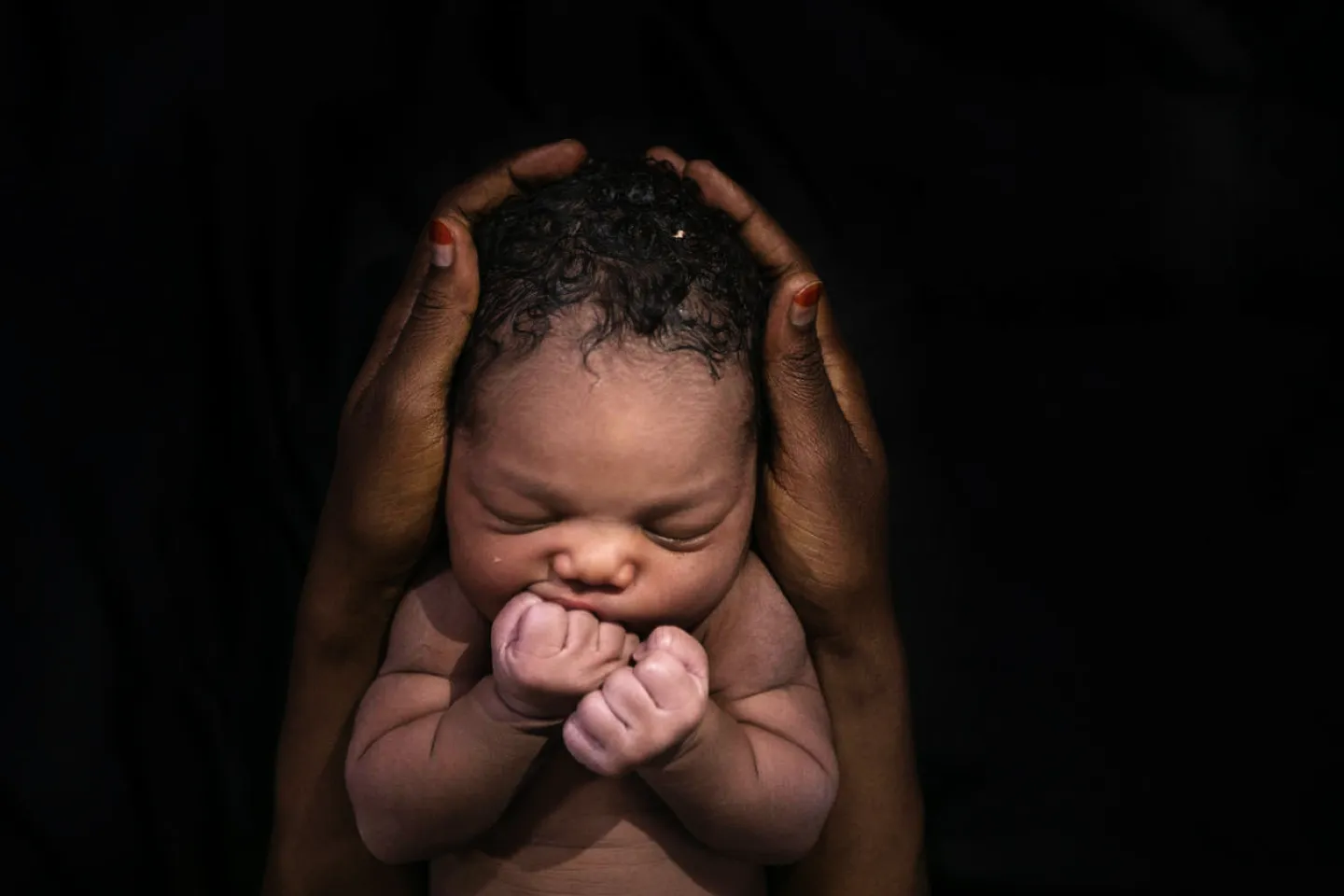 A newborn puts her fists to her mouth