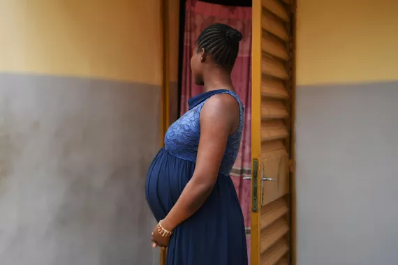 A pregnant woman holds her belly and looks away from the camera